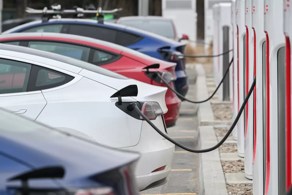 Close-up of four Tesla sedans parked and plugged in at charging station.